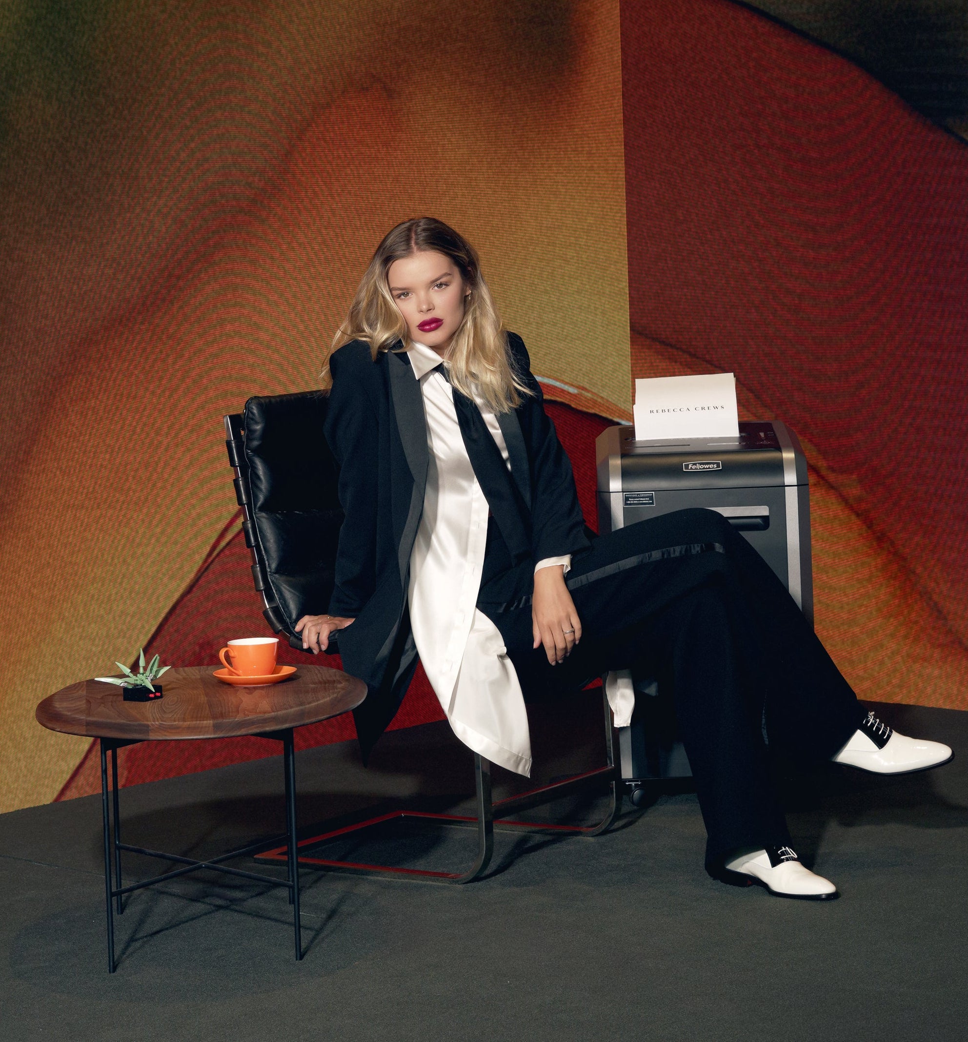 Woman in a black suit sitting in a chair with a colorful abstract painting in the background